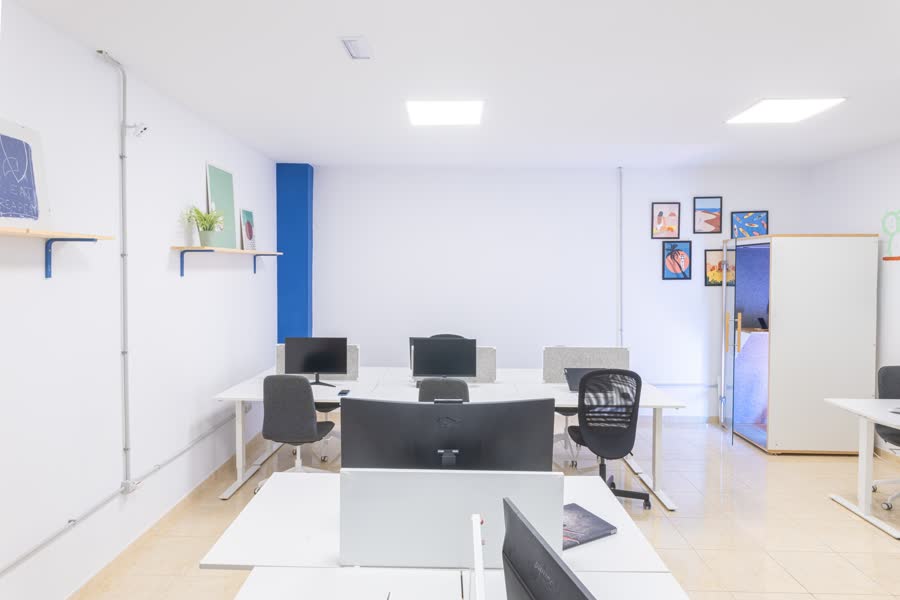 The FICO coworking room: rows of white desks with monitors, ergonomic chairs and the phone booth against the far wall