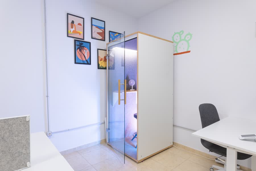 The soundproof phone booth in the corner of the room, prints on the wall beside it